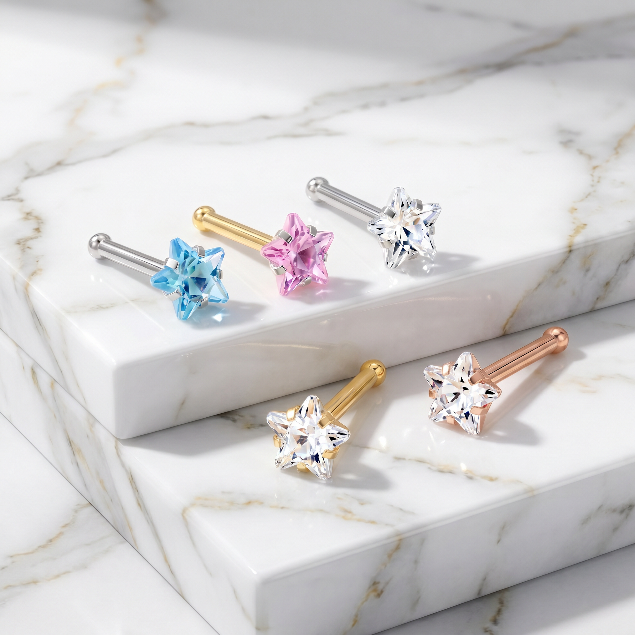 Five star-shaped stud earrings with faceted gemstones in blue, pink, clear, rose gold, and yellow gold tones, displayed on white marble blocks.