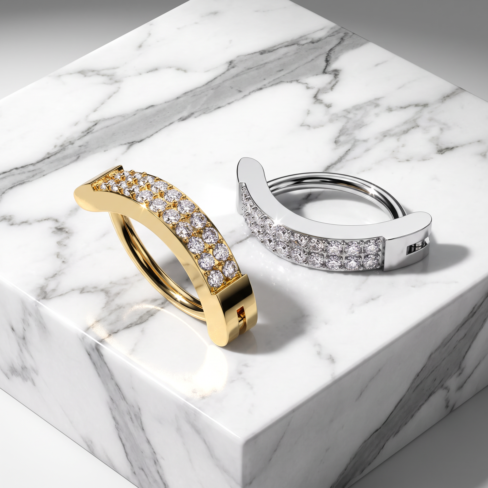 Two curved hoop-style rings with rows of clear stones, one in yellow gold and one in white gold or platinum, displayed on a white marble block.