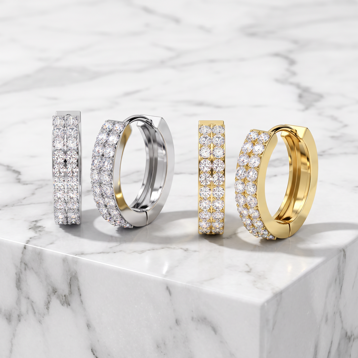 Four huggie hoop earrings displayed on a white marble slab. Two earrings are silver-toned with pavé-set clear stones, and two are gold-toned with pavé-set clear stones.