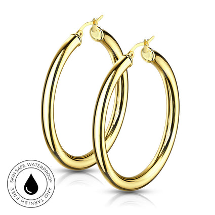 A pair of thick, polished gold hoop earrings shown on a clean white background with a subtle reflection. A circular badge in the bottom-left corner reads 'SKIN SAFE WATERPROOF AND TARNISH FREE' with a black water droplet icon.