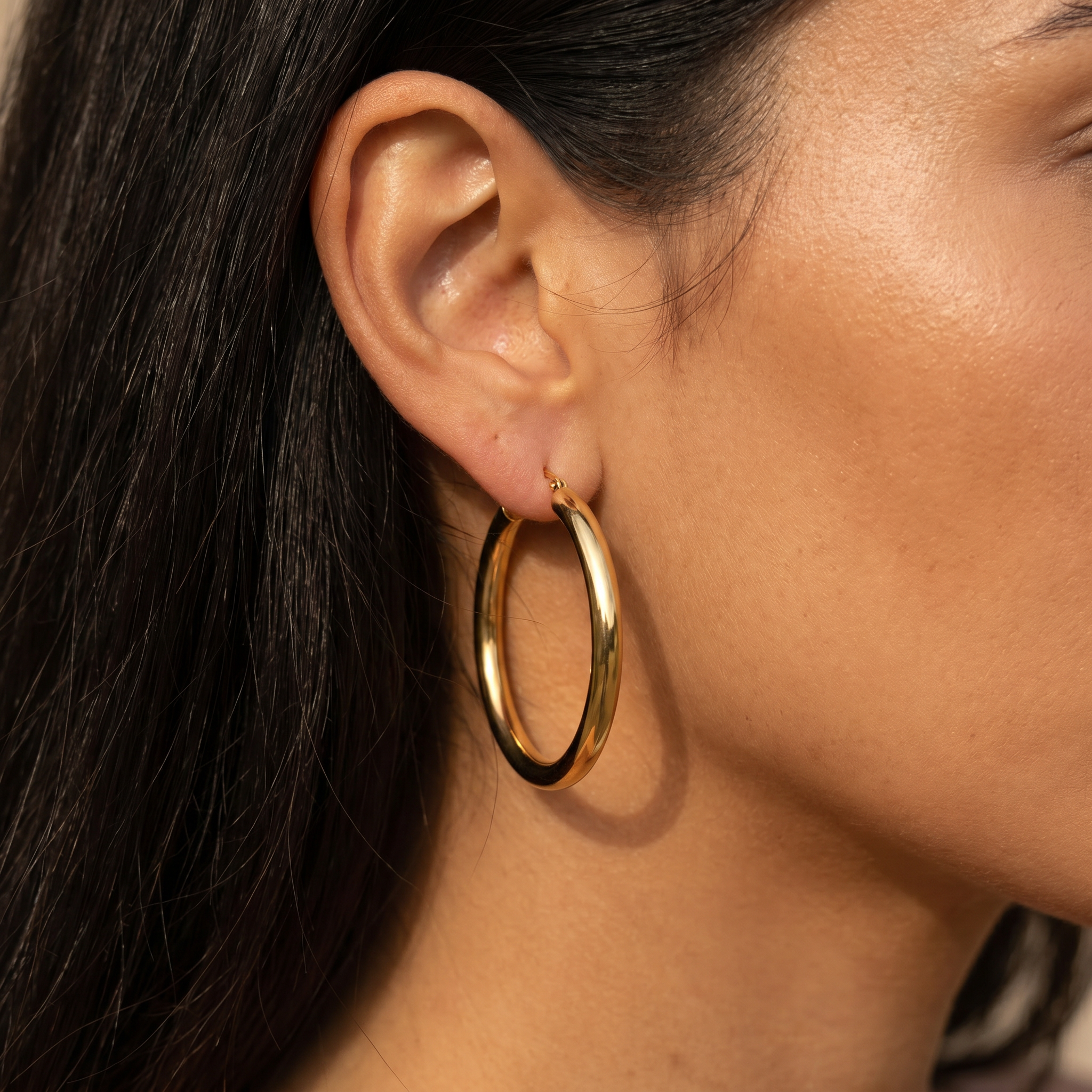 A close-up of a model's ear wearing a thick, polished gold hoop earring.