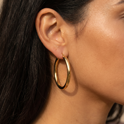 A close-up of a model's ear wearing a thick, polished gold hoop earring.