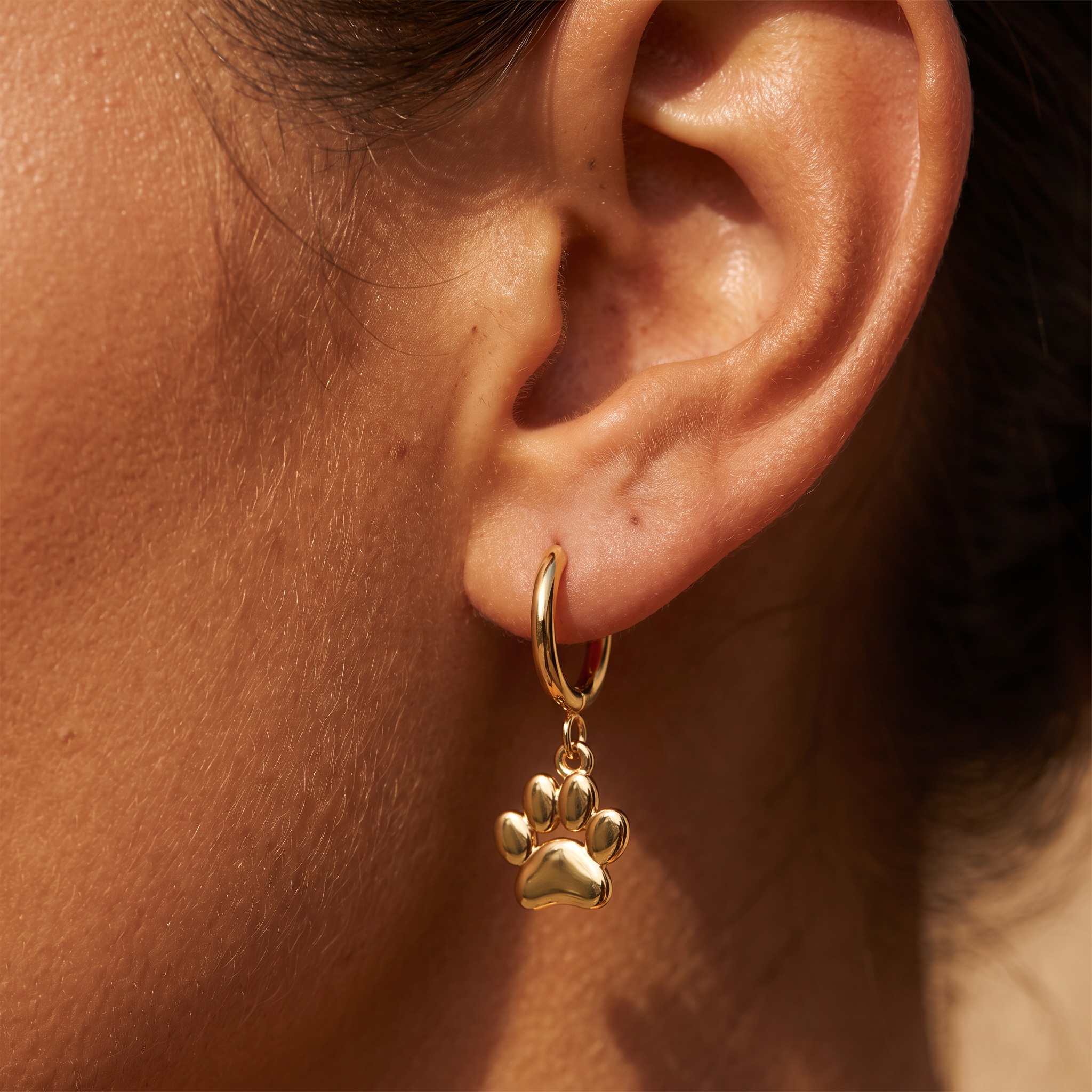 A close-up of a person's ear wearing a gold hoop earring with a dangling paw print charm.