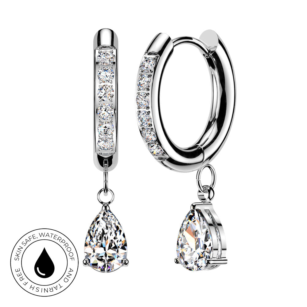 Silver huggie hoop earrings with clear pavé stones and teardrop-shaped clear gemstone drops, shown on a white background with a circular skin-safe waterproof badge.