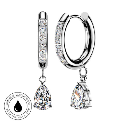 Silver huggie hoop earrings with clear pavé stones and teardrop-shaped clear gemstone drops, shown on a white background with a circular skin-safe waterproof badge.