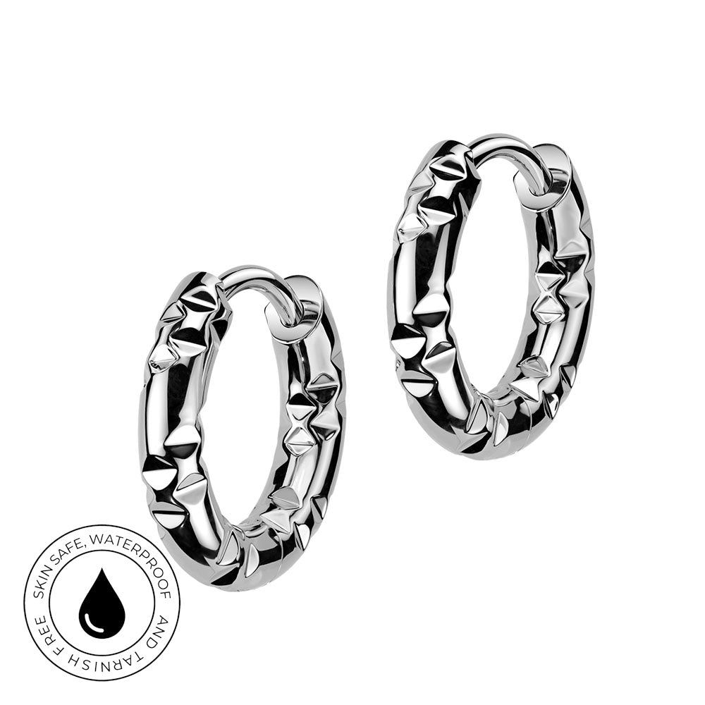 A pair of silver huggie hoop earrings with a textured, faceted outer surface, shown on a plain white background with a circular 'Skin Safe Waterproof' badge in the bottom-left corner.