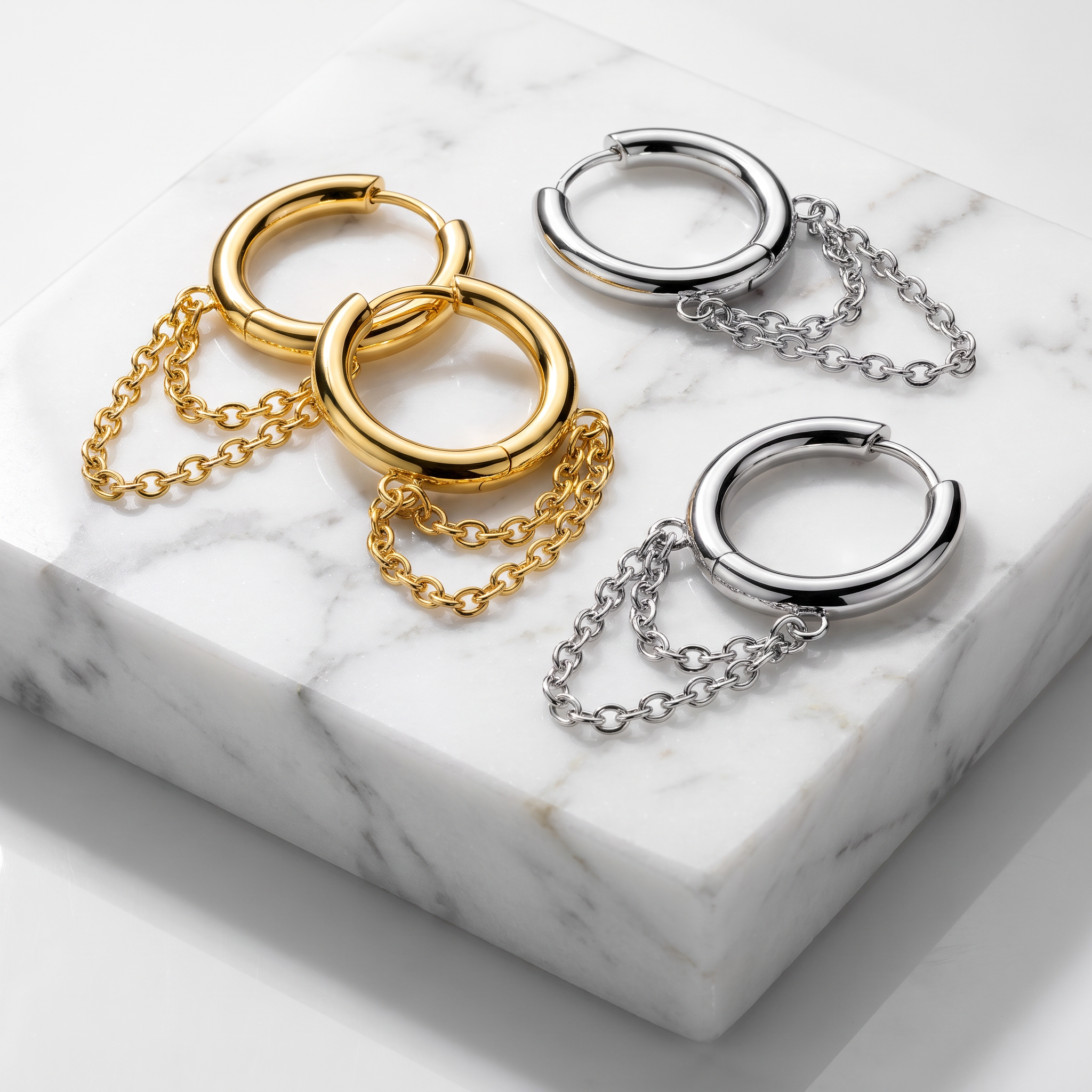 Three pairs of hoop earrings with dangling chain accents, shown in gold and silver finishes on a white marble slab.