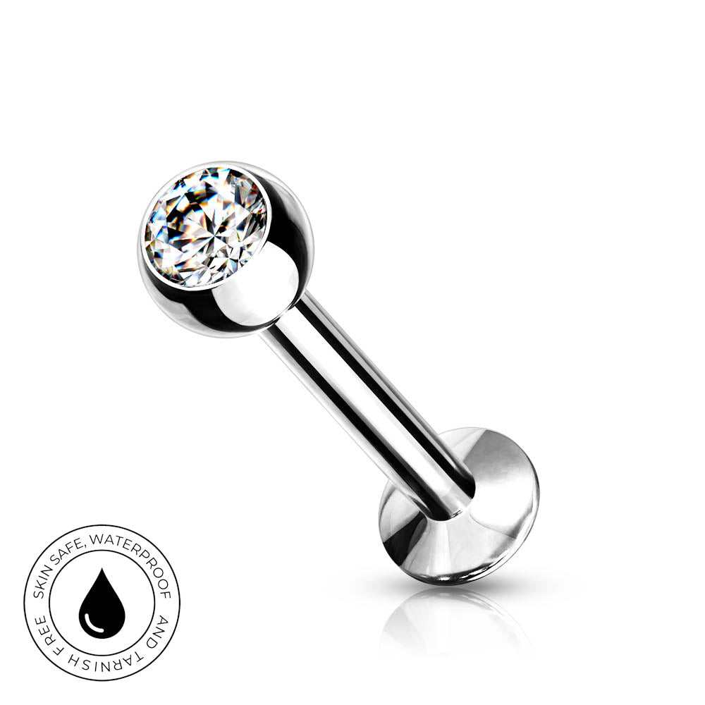A silver-toned labret piercing barbell with a clear faceted gemstone ball, shown on a white background with a circular 'Skin Safe Waterproof' badge in the lower-left corner.