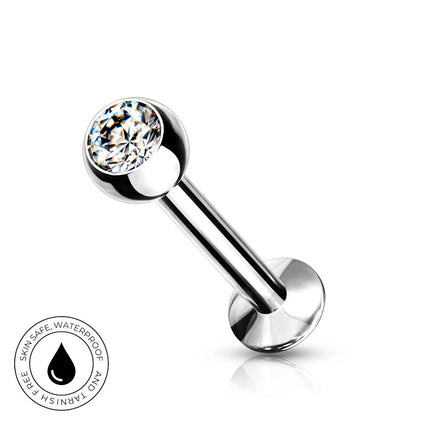 A silver-toned labret piercing barbell with a clear faceted gemstone ball, shown on a white background with a circular 'Skin Safe Waterproof' badge in the lower-left corner.