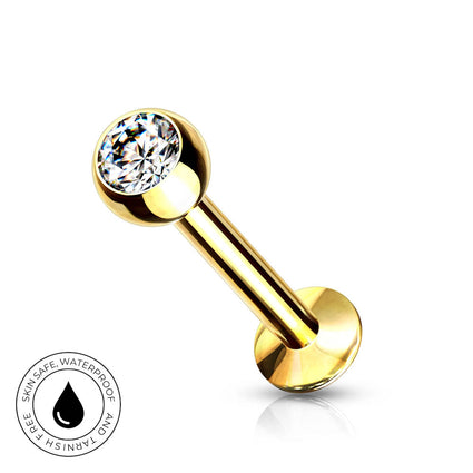 A gold-plated labret piercing barbell with a clear round-cut gemstone on the end, shown on a white background with a circular 'Skin Safe Waterproof' badge in the bottom-left corner.