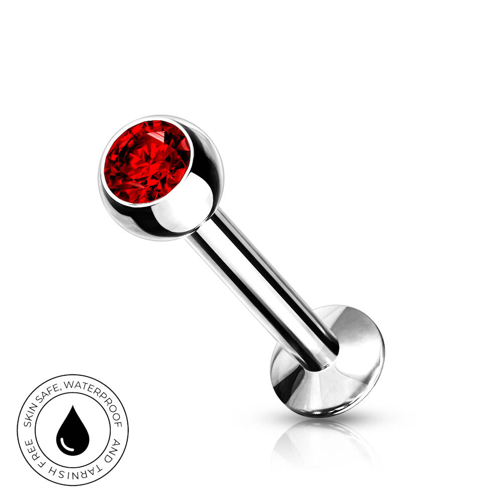 A silver-toned labret piercing barbell with a faceted red gemstone ball end, shown on a clean white background with a small circular 'skin-safe waterproof' badge in the lower left corner.