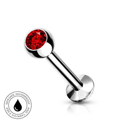 A silver-toned labret piercing barbell with a faceted red gemstone ball end, shown on a clean white background with a small circular 'skin-safe waterproof' badge in the lower left corner.