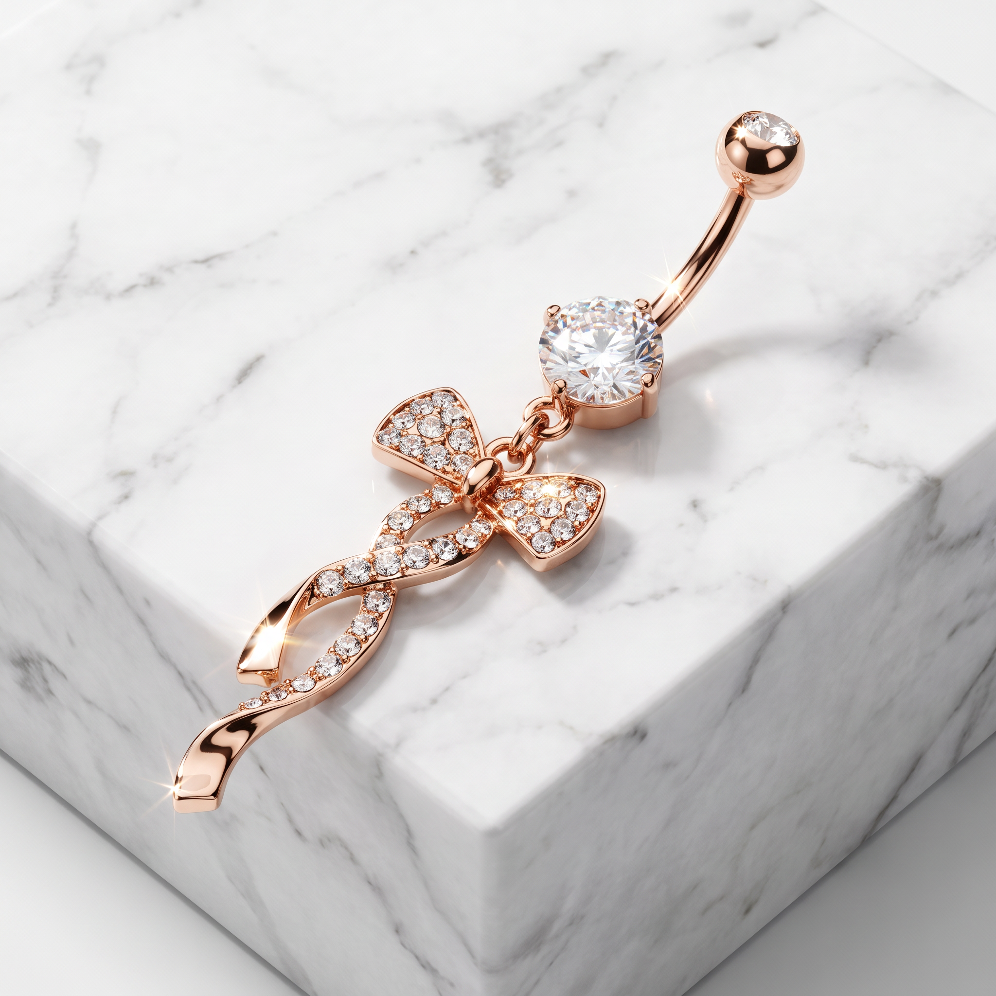 Rose gold navel piercing jewelry with a bow and ribbon charm design, set with clear crystals, displayed on a white marble block.