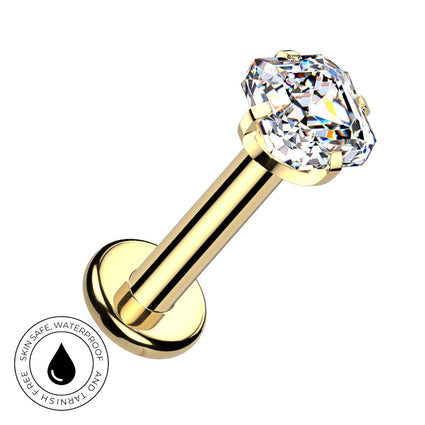 A gold-plated labret piercing barbell with a large, clear, cushion-cut gemstone on a plain white background. A circular graphic overlay in the bottom-left corner features a water droplet icon and the text 'SKIN SAFE WATERPROOF AND TARNISH FREE'.