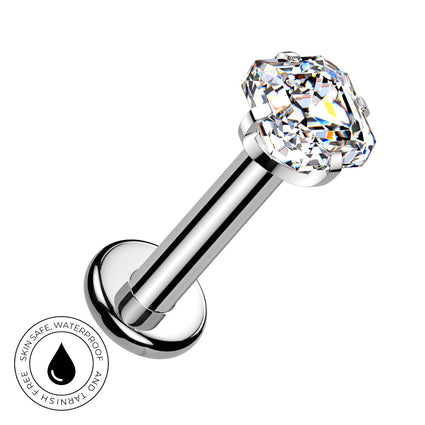 A silver-toned labret piercing barbell with a large, clear, faceted gemstone on the end. The image is set against a plain white background with a circular graphic overlay in the bottom-left corner that reads 'SKIN SAFE WATERPROOF' with a water droplet icon.