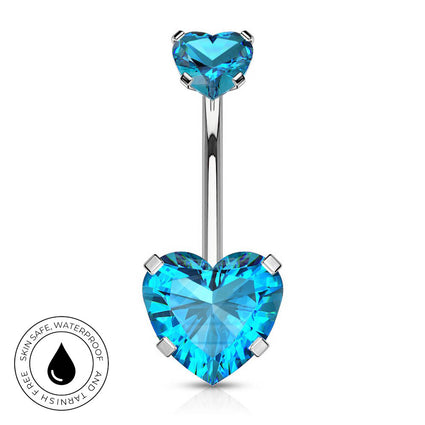 A silver-toned navel barbell piercing with a large, faceted light blue heart-shaped crystal at the bottom and a smaller matching blue heart at the top. A circular graphic in the lower-left corner highlights skin-safe, waterproof properties.
