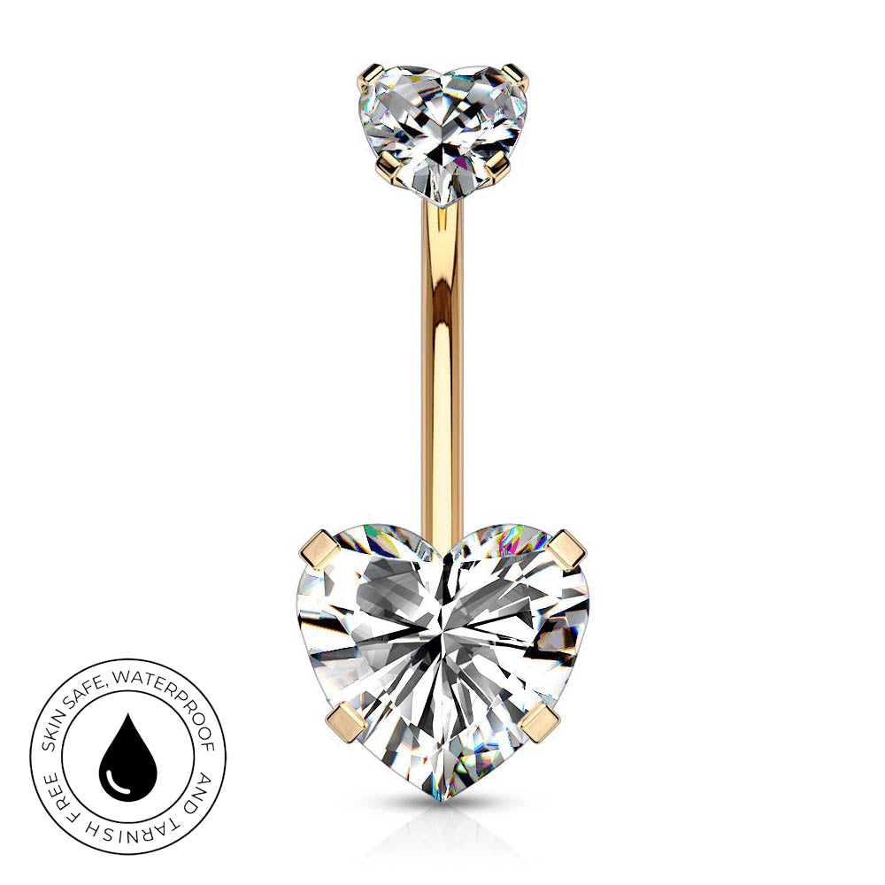 Gold heart-shaped barbell navel jewelry with a large clear heart gemstone and a smaller heart gemstone at the top, shown on a white background with a circular skin-safe waterproof badge in the lower left.