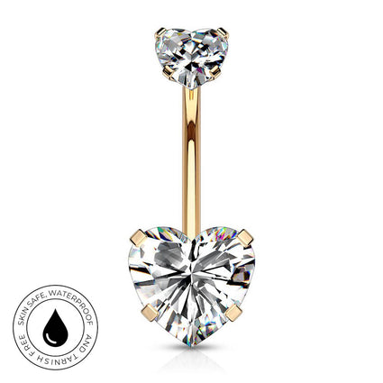 Gold heart-shaped barbell navel jewelry with a large clear heart gemstone and a smaller heart gemstone at the top, shown on a white background with a circular skin-safe waterproof badge in the lower left.