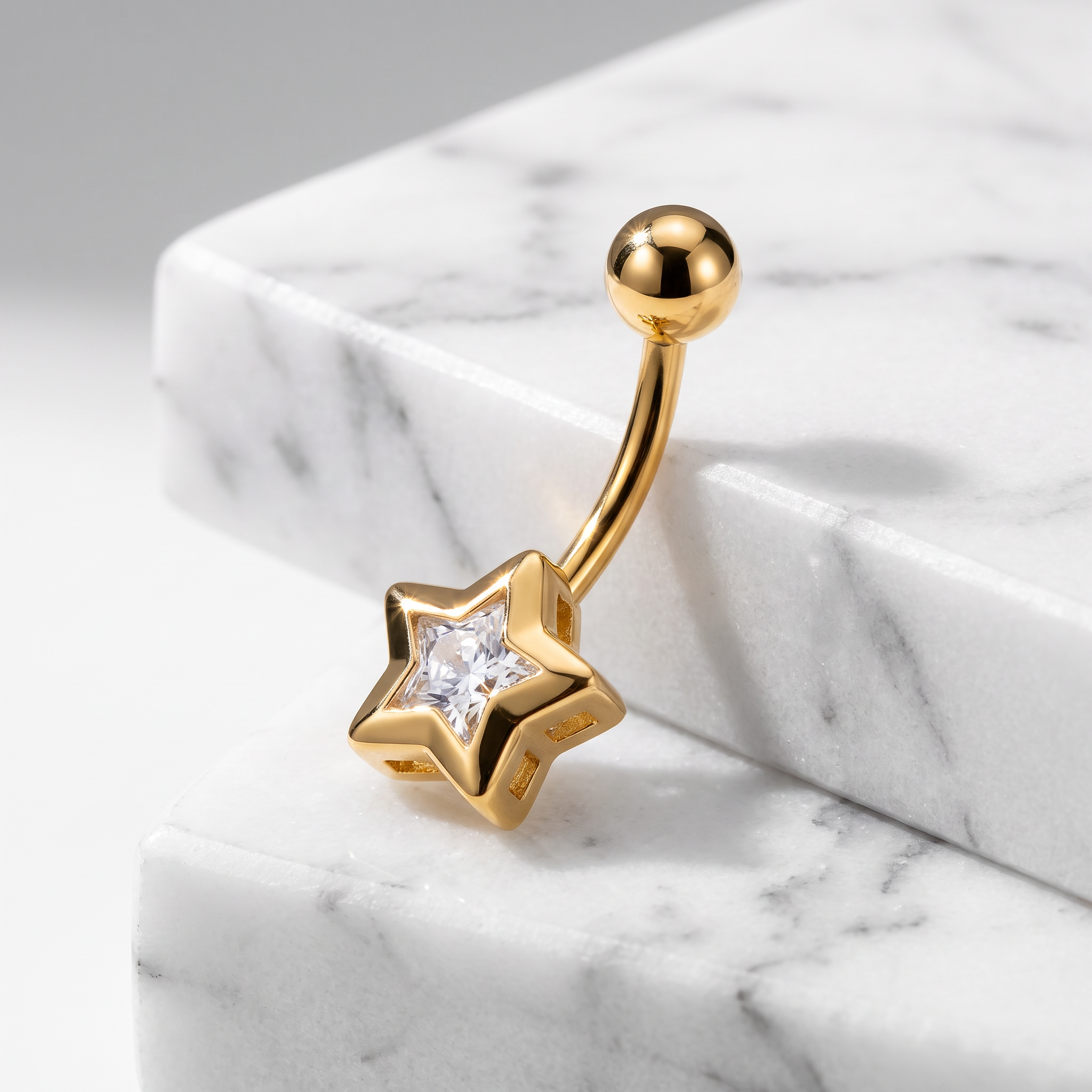 Gold star-shaped belly button ring with a clear central gemstone, displayed on a white marble block.