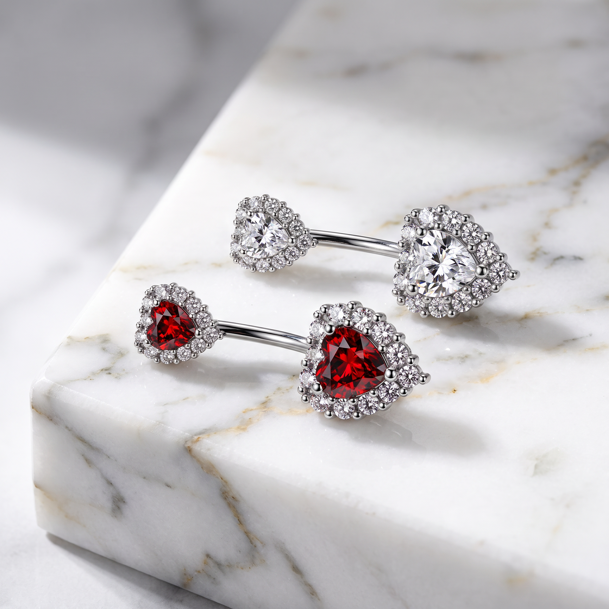 Three silver-toned belly button rings with heart-shaped red gemstones and clear halo stones, arranged on a white marble block.