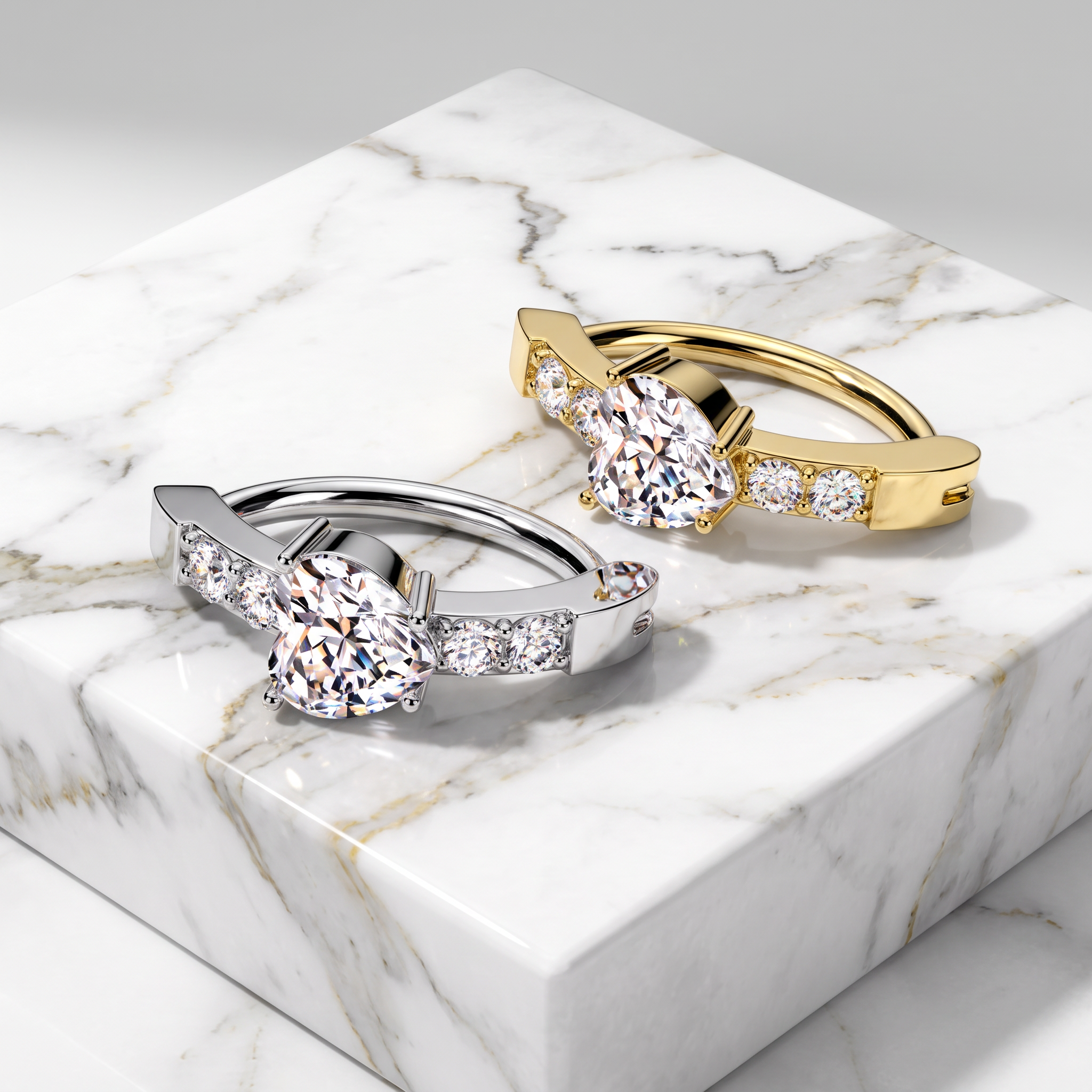 Two solitaire-style rings with large round clear stones and smaller accent stones, shown on a white marble block. One ring is silver-toned and the other is yellow gold-toned.