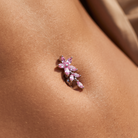 A close-up of a pink gemstone flower-shaped navel piercing stud worn on a person's lower abdomen.
