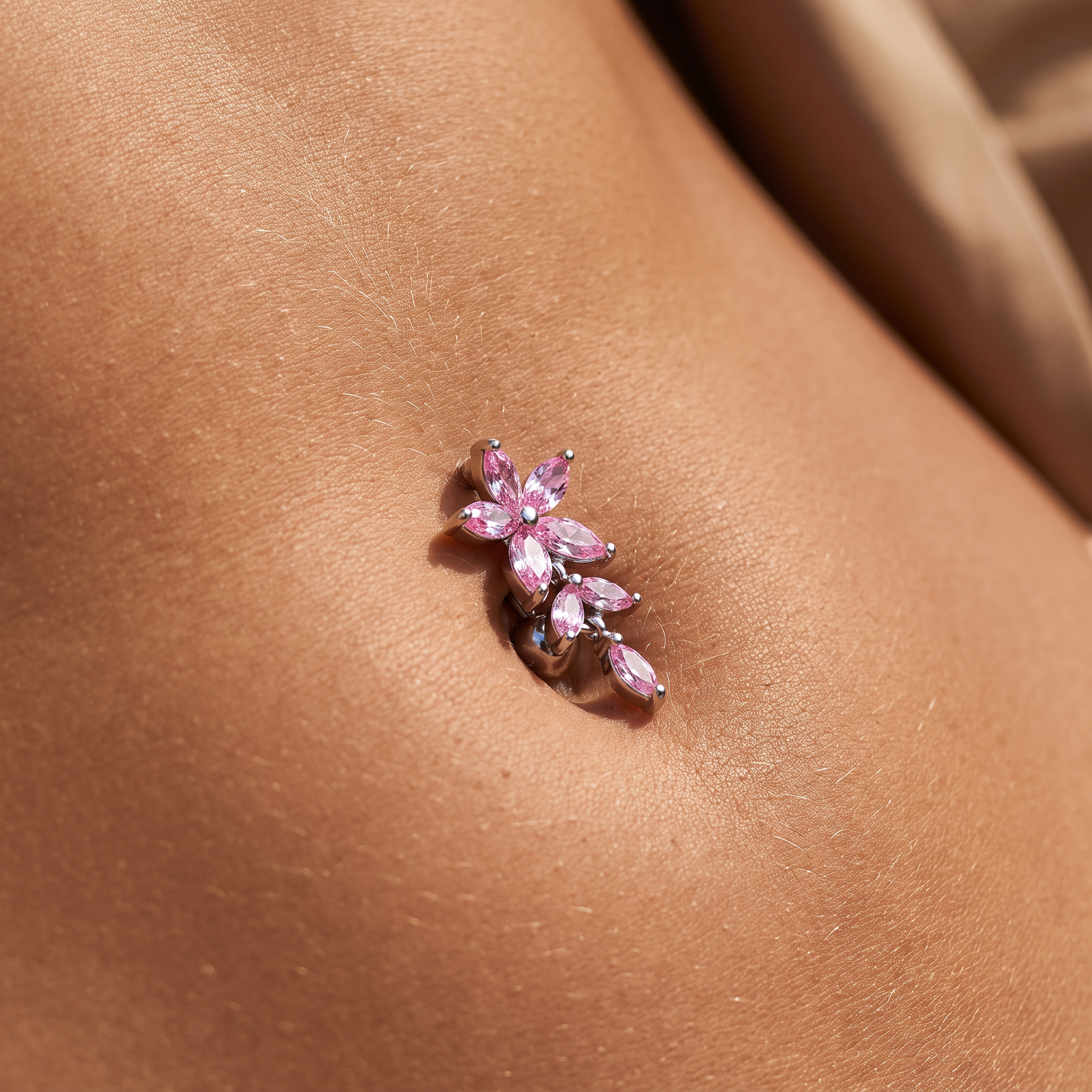 A close-up of a pink gemstone flower-shaped navel piercing stud worn on a person's lower abdomen.