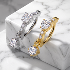 Two huggie hoop earrings with dangling round-cut gemstones, shown on a white marble block. One earring is silver-toned and the other is gold-toned, both accented with small pavé-set stones.