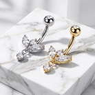 Two belly button rings with butterfly and drop crystal designs, one in silver and one in gold, displayed on a white marble block.