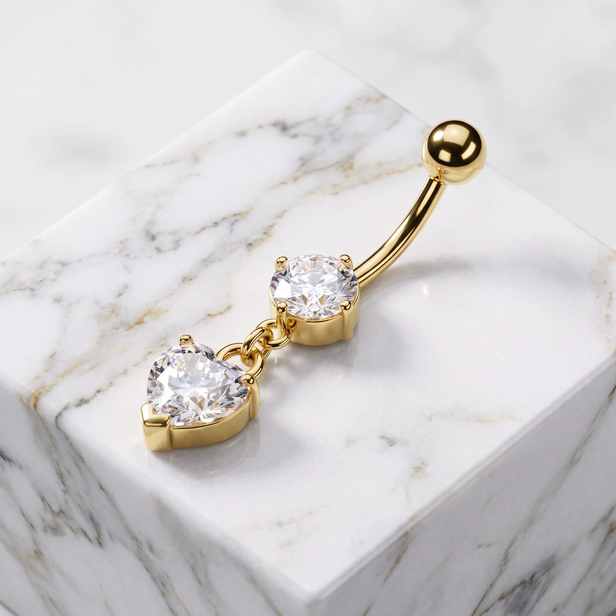 Gold-plated belly button ring with two clear heart-shaped gemstones, displayed on a white marble block.