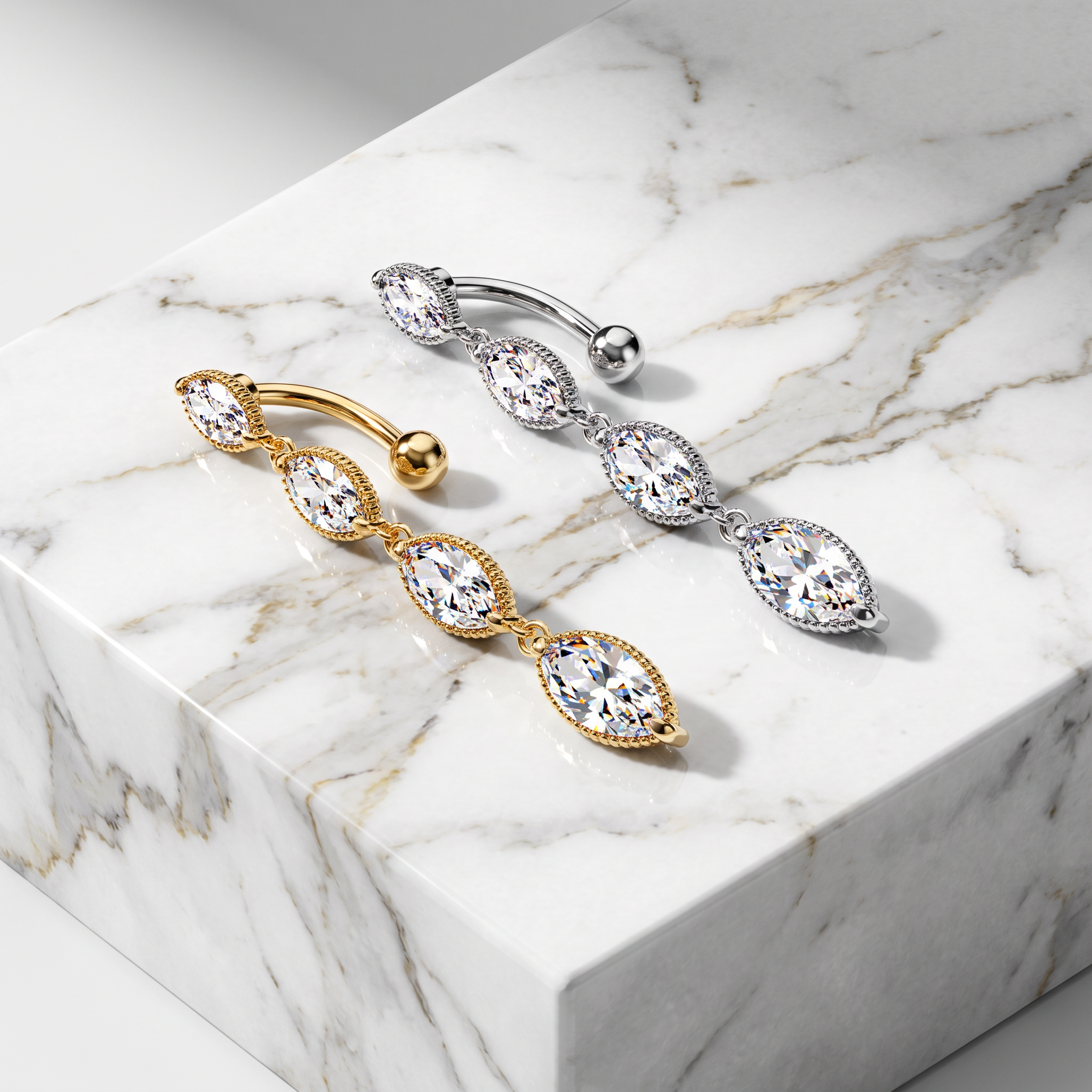 Two triple-stone belly button rings displayed on a white marble block. One ring is gold with marquise-cut clear stones, and the other is silver with marquise-cut clear stones.