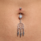A silver belly button ring with a dreamcatcher charm and three dangling feathers, shown on a person's navel.