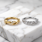 Two rings displayed on a white marble block: a yellow gold ring with diamond accents and a silver ring with textured pavé-style diamond settings.