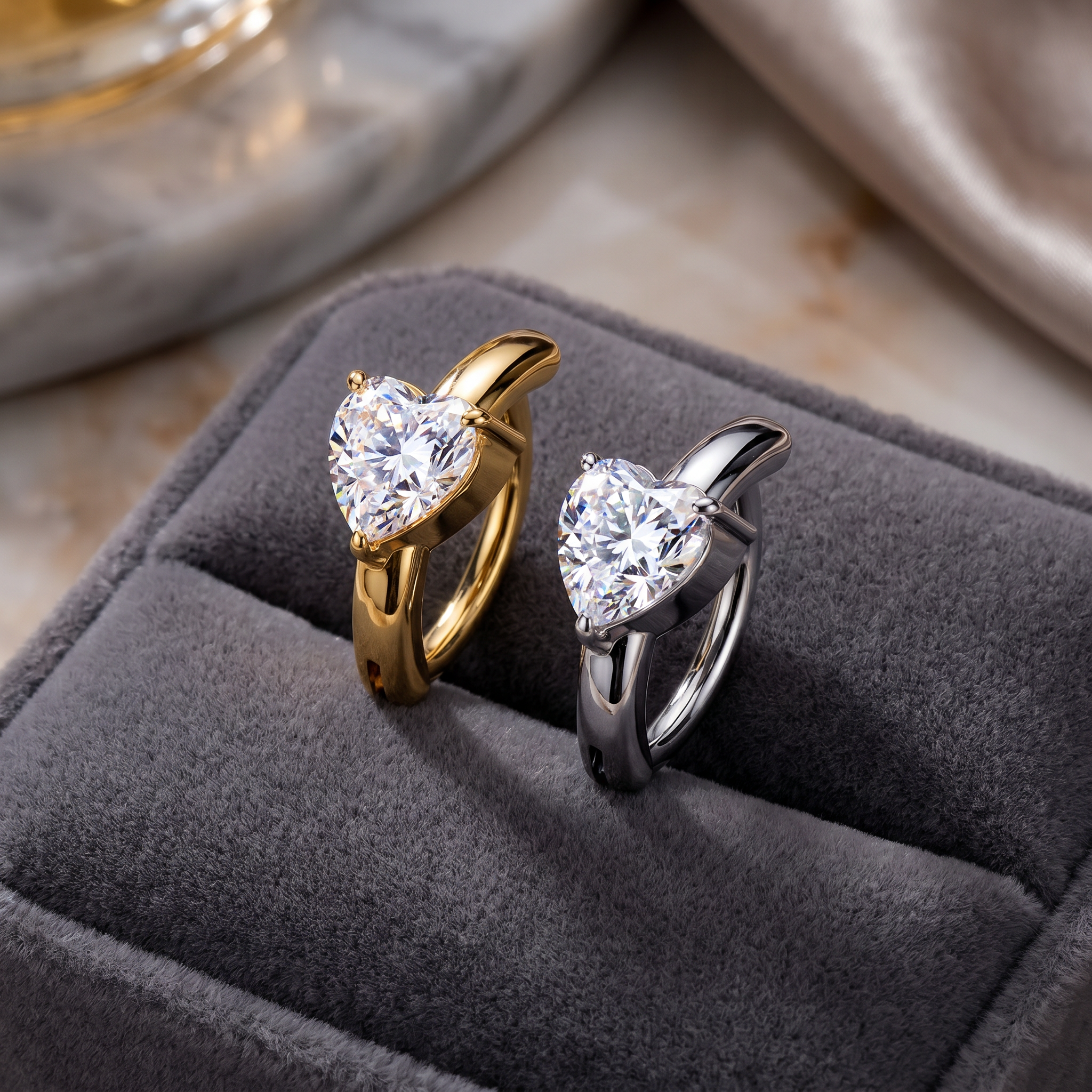 Two heart-shaped solitaire rings, one in yellow gold and one in silver, displayed on a dark gray velvet ring box.