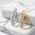 Two huggie hoop earrings with heart-shaped clear gemstones, one in silver and one in yellow gold, displayed on a white marble block.