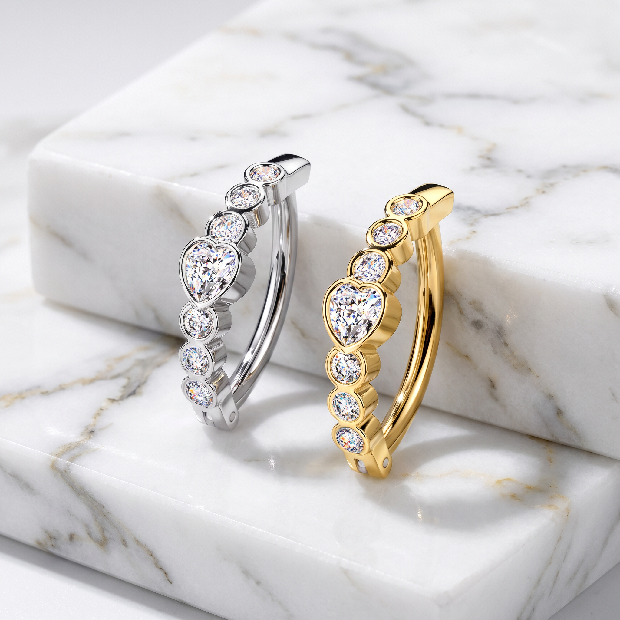 Two huggie hoop earrings with heart-shaped clear gemstones, one in silver and one in yellow gold, displayed on a white marble block.