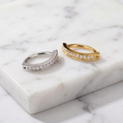 Two slim huggie hoop rings with pavé-set clear stones, one in silver-tone metal and one in yellow gold-tone metal, displayed on a white marble slab.