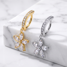 Two flower-shaped hoop earrings with marquise-cut clear stones are displayed on a white marble block. One earring is gold-toned and the other is silver-toned, both with rows of small clear stones along the hoop.