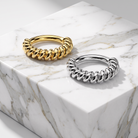 Two twisted rope-style rings, one gold and one silver, displayed on a white marble block.