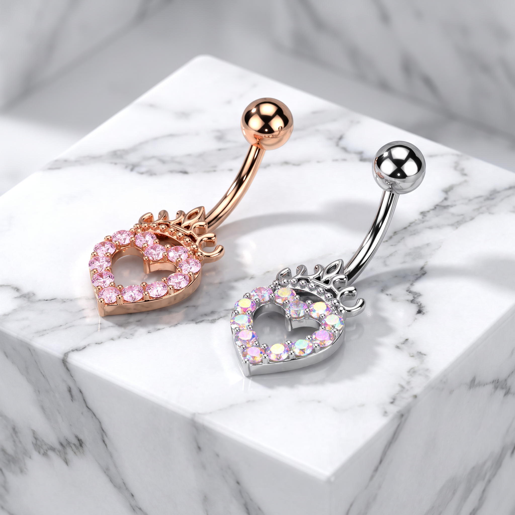 Two belly button rings displayed on a white marble block. One ring is rose gold with a pink heart-shaped crystal charm, and the other is silver with a pink heart-shaped crystal charm.