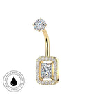 Gold curved barbell navel piercing ring with a rectangular halo of small clear stones and a central princess-cut clear stone, shown on a white background with a small circular skin-safe waterproof badge in the lower left.