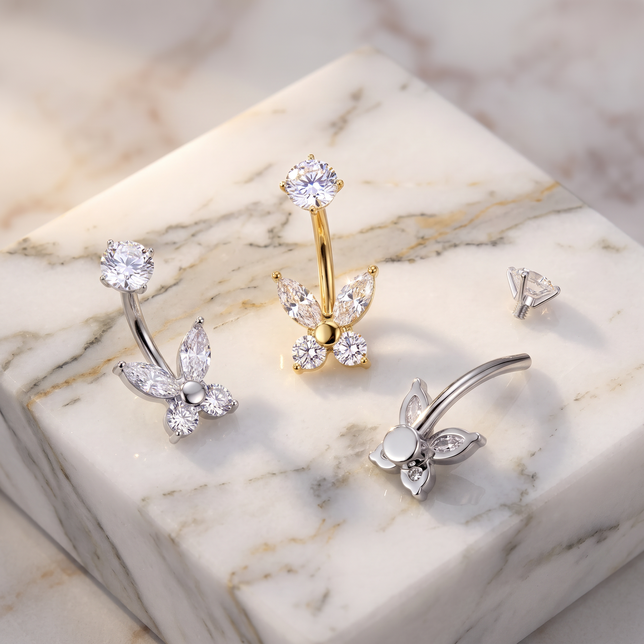 Three butterfly-shaped nose rings with clear crystal gemstones, shown in silver and gold metal finishes, arranged on a white marble display block.