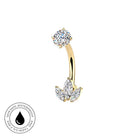 Gold curved barbell piercing stud with a round clear gemstone on one end and a three-stone leaf cluster on the other, shown on a white background with a circular skin-safe waterproof badge in the lower left.