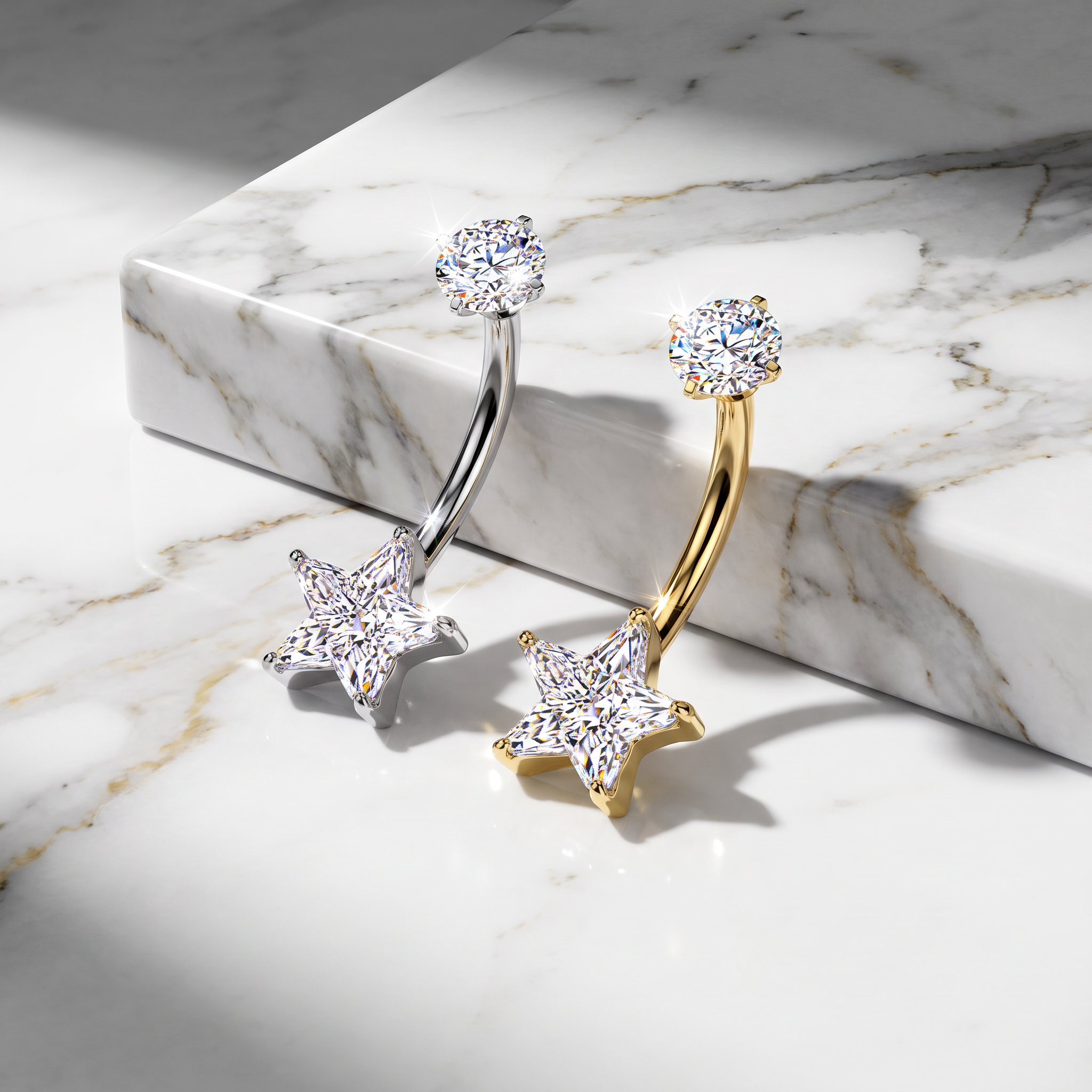Two curved barbell belly button piercings with star-shaped studs, one in silver and one in yellow gold, both set with clear cubic zirconia stones, displayed on a white marble block and marble surface.