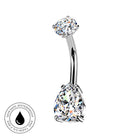 A curved barbell belly button ring with a large pear-cut clear gemstone and a smaller oval-cut clear gemstone, shown on a white background with a circular 'Skin Safe Waterproof' badge in the lower left corner.