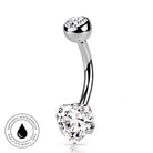 A curved barbell belly button piercing with a heart-shaped clear gemstone at the bottom and a round clear gemstone at the top, shown on a white background with a circular 'Skin Safe Waterproof' badge in the lower left.