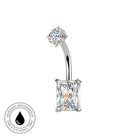 A silver-toned curved barbell navel piercing jewelry piece featuring a round clear gemstone on the top and a rectangular clear gemstone on the bottom, shown on a white background with a circular 'Skin Safe Waterproof' badge in the lower-left corner.