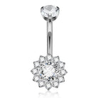 A silver-toned navel ring featuring a single round clear gemstone at the top and a flower-shaped halo cluster with multiple clear stones at the bottom, shown on a white background.