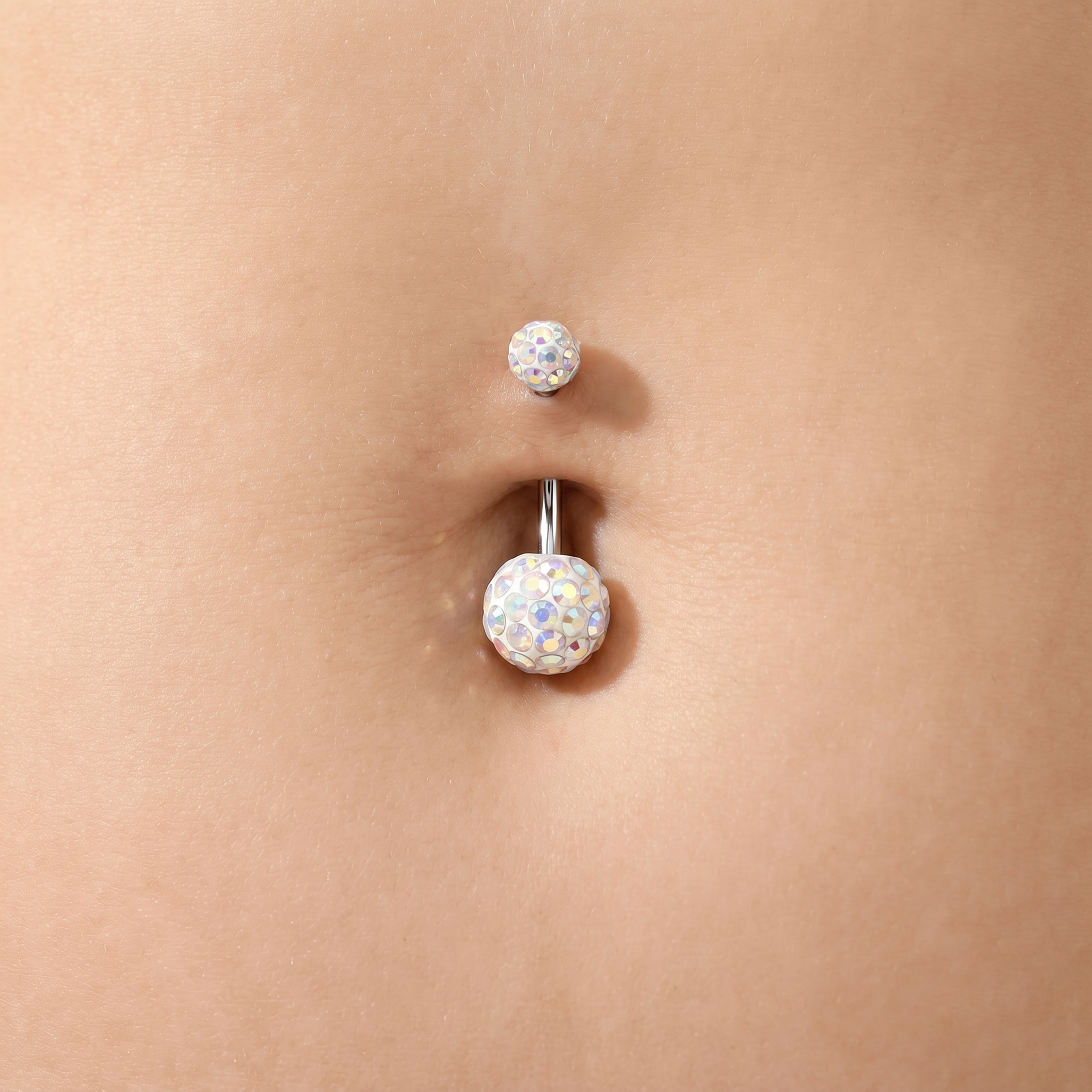 A close-up of a belly button with a silver-toned navel piercing. The lower stud features a large, round, iridescent white cabochon gemstone, while the upper stud has a smaller, similar round gemstone.