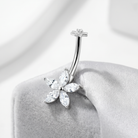 A silver-toned curved barbell belly button ring with a five-petal flower setting made of clear marquise-cut stones, displayed on a soft gray jewelry stand.